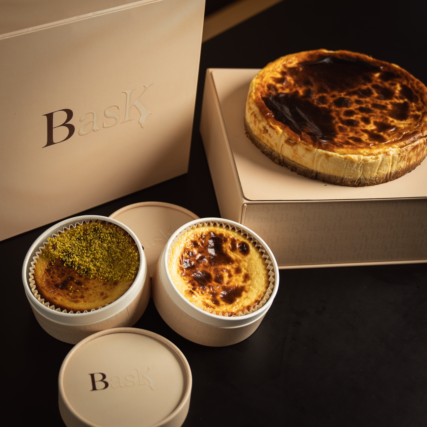 The collection of Bask Dubai Cheesecake boutique assortment. Including a large Basque cheesecake and two small size cheesecakes, traditional and pistachio flavors.