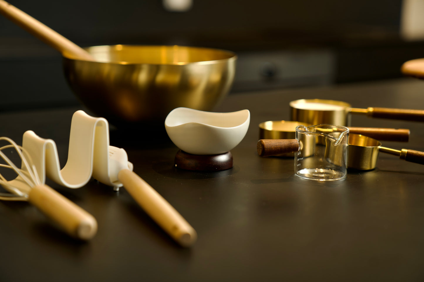 Set of elegant premium bakery utensils including a whisk, bowls, and measuring cups on a dark surface.