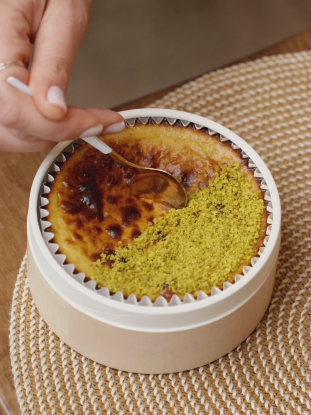 A close up showing a spoon digging into a Luxury Basque Pistachio Cheesecake by Bask Dubai, showing a very creamy cheesecake inside, a praline pistachio layer and a short bread crunchy base.